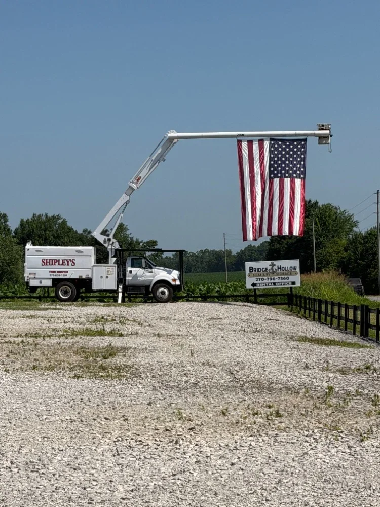 Aerial lift truck with extended boom displaying large American flag on horizontal support beam